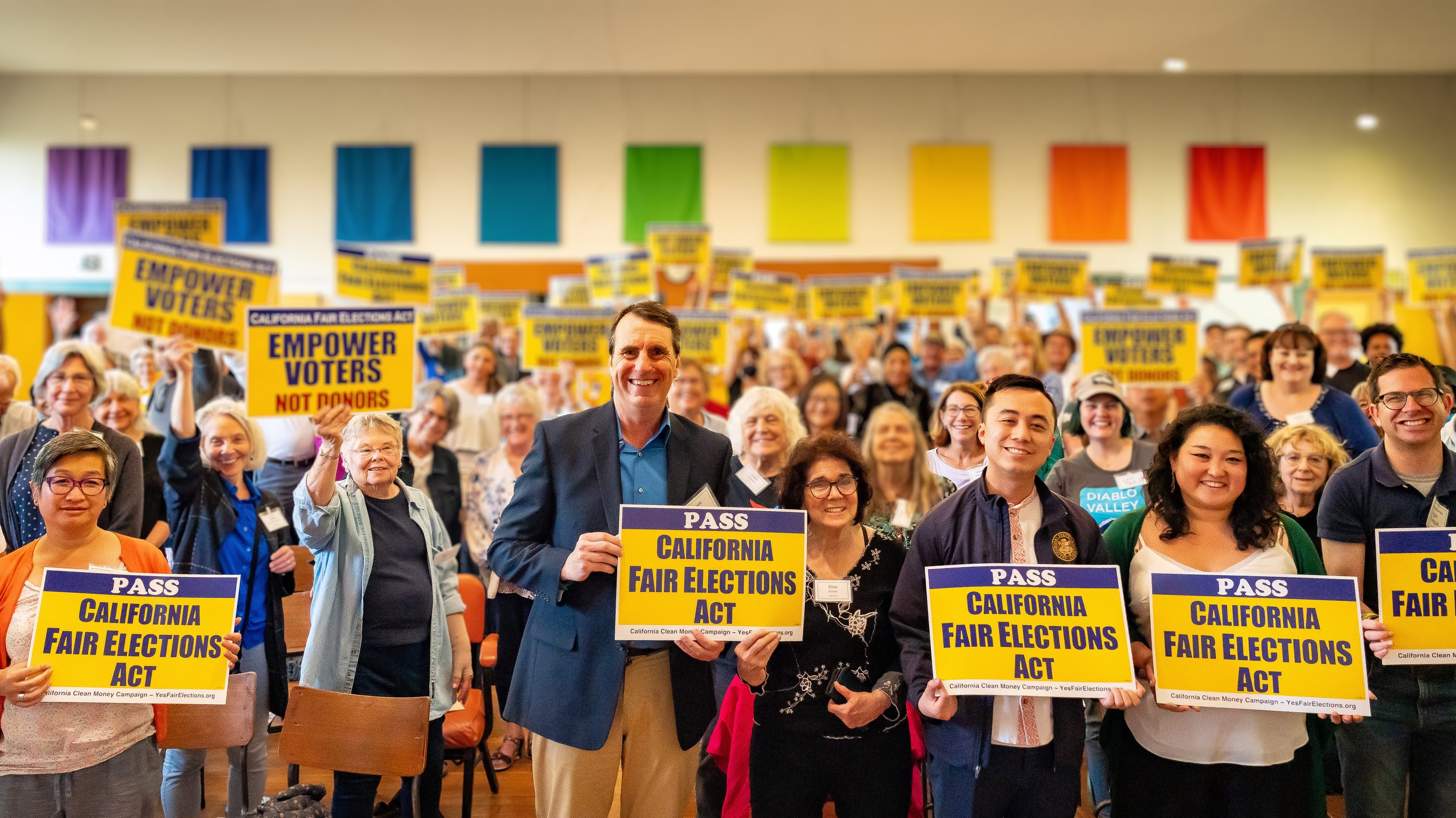 A hall packed with supporters holding Pass the California Fair Elections Act signs